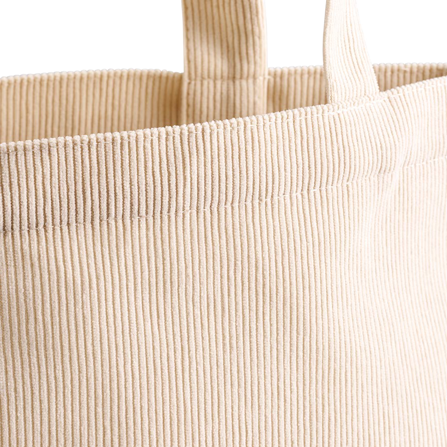 秋冬の装いにすっと寄り添う、あたたかみのあるコーデュロイ素材を使用したトートバッグです。細かな畝(うね)が生み出す陰影が、シンプルなフォルムに上品な表情と季節感を添え、ニットやコート、デニムといった秋冬コーディネートに自然になじみます。生地の内側には不織布を貼り合わせることで、ほどよい厚みとしっかりとしたハリを実現。使い込んでもくたっとへたりにくく、デスクやテーブルに置いたときも角がきれいに立ち上がり、美しいシルエットをキープします。自立感のあるかたちなので中の荷物が見渡しやすく、書類やタブレット、お弁当箱やペットボトルもすっきりと収まり、荷物の出し入れもスムーズ。通勤・通学のサブバッグやランチバッグ、ちょっとしたお出かけのお供として毎日活躍する一枚です。やわらかなアイボリーベージュのナチュラルカラーは男女問わず使いやすく、名入れやオリジナルプリントを施したノベルティ・販促品、記念品やギフトとしてもおすすめです。